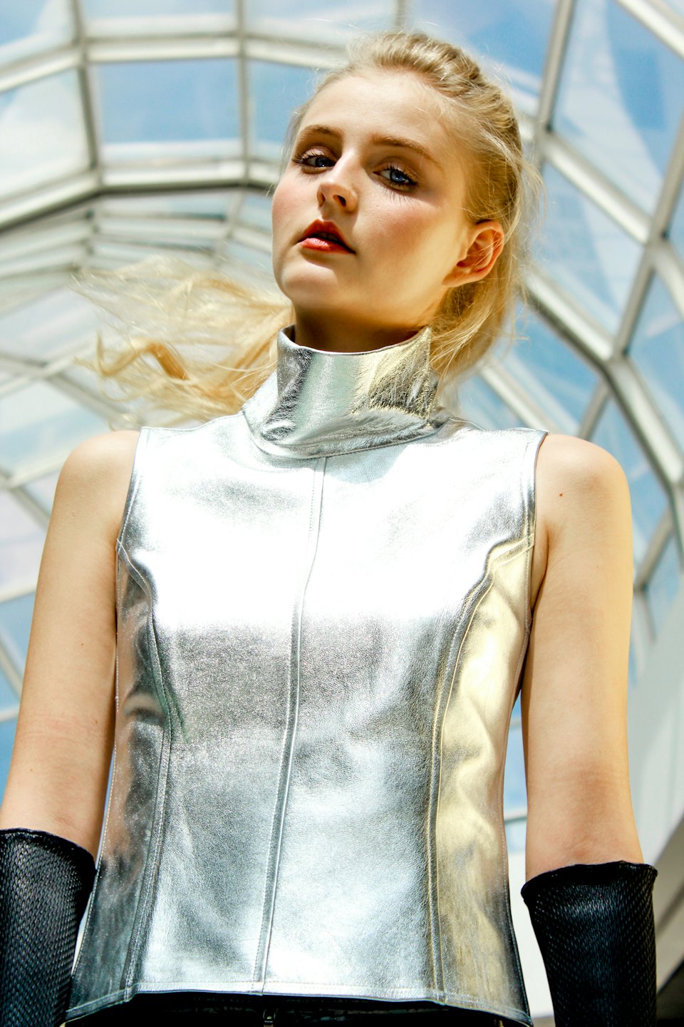 Woman in a silver top posing near a glass ceiling.