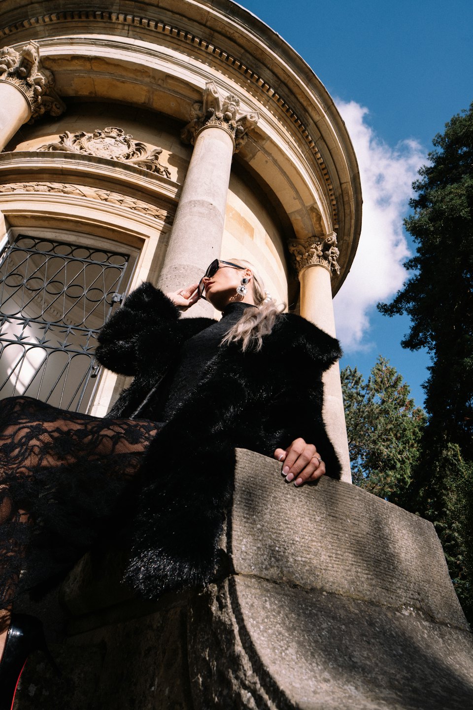 Woman in a black fur coat posing before stone columns.