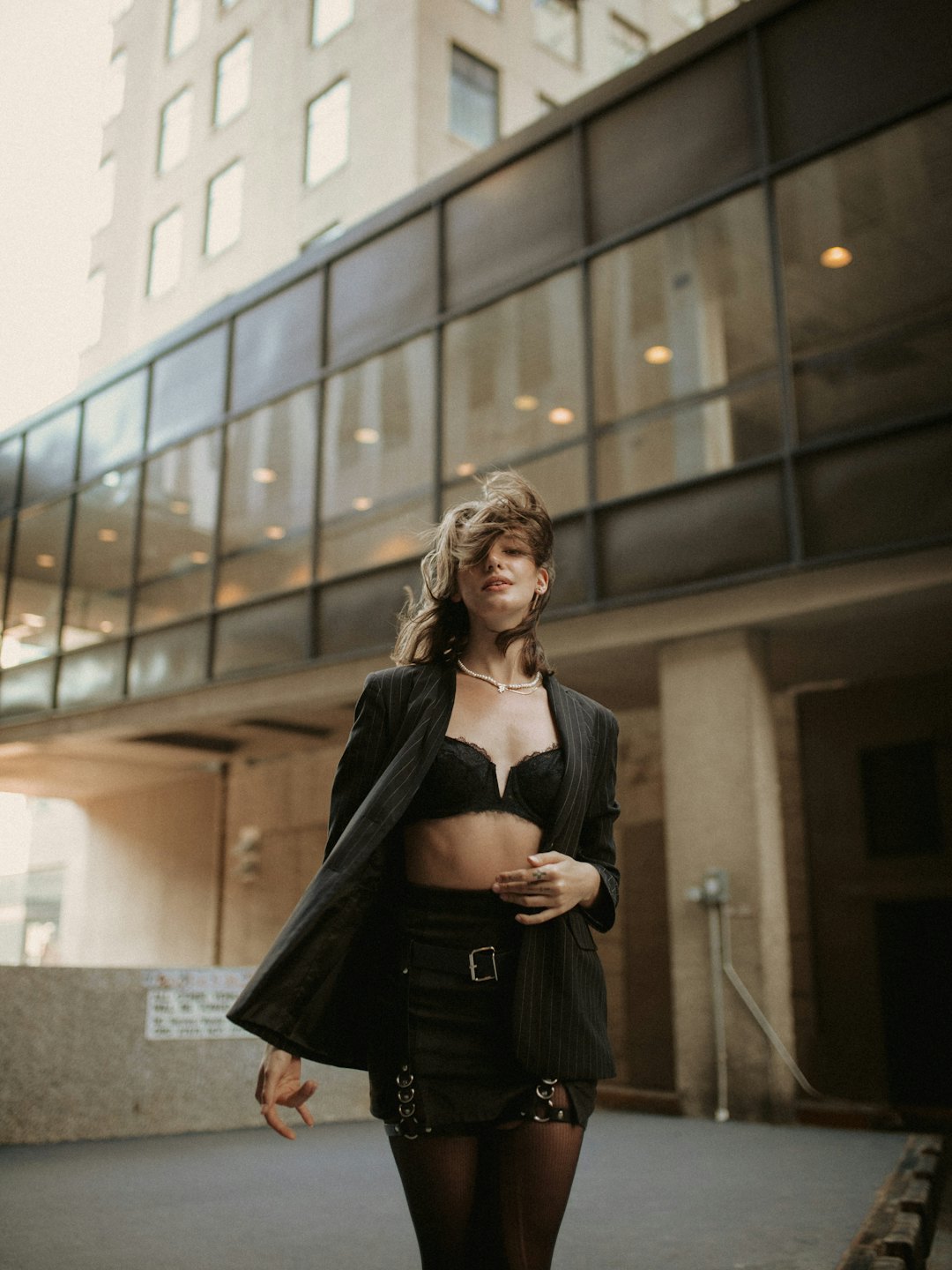 Woman in blazer and skirt stands by modern building.
